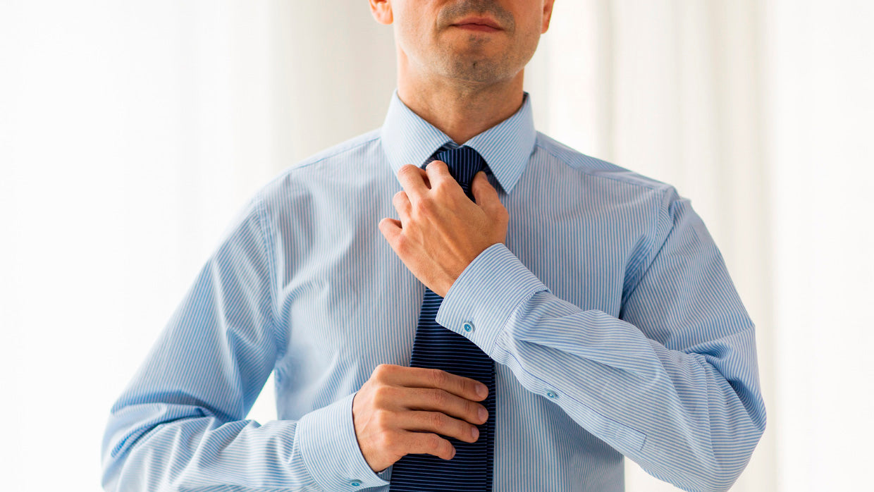 Close-up of a man's hands tying a classic Windsor knot on a navy blue tie