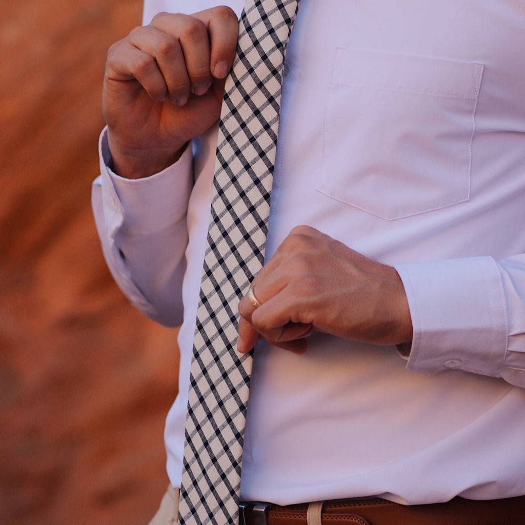Person adjusting a checkered tie on a white shirt with a blurred background