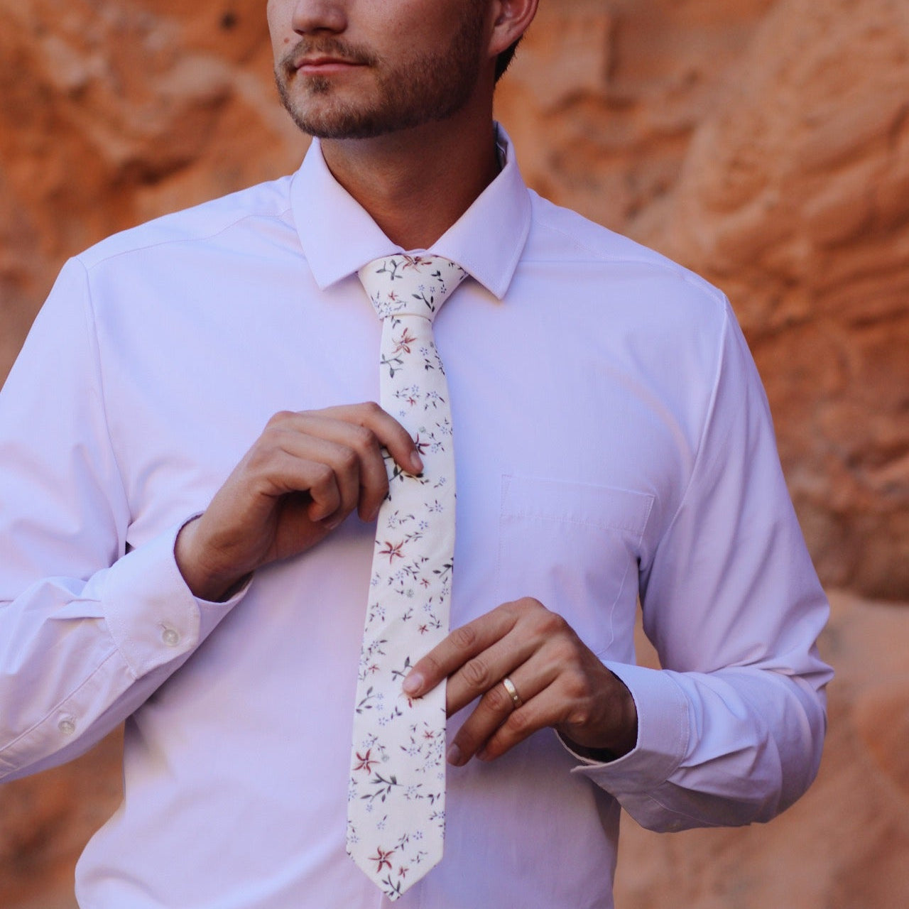 Man adjusting a floral tie against a desert background
