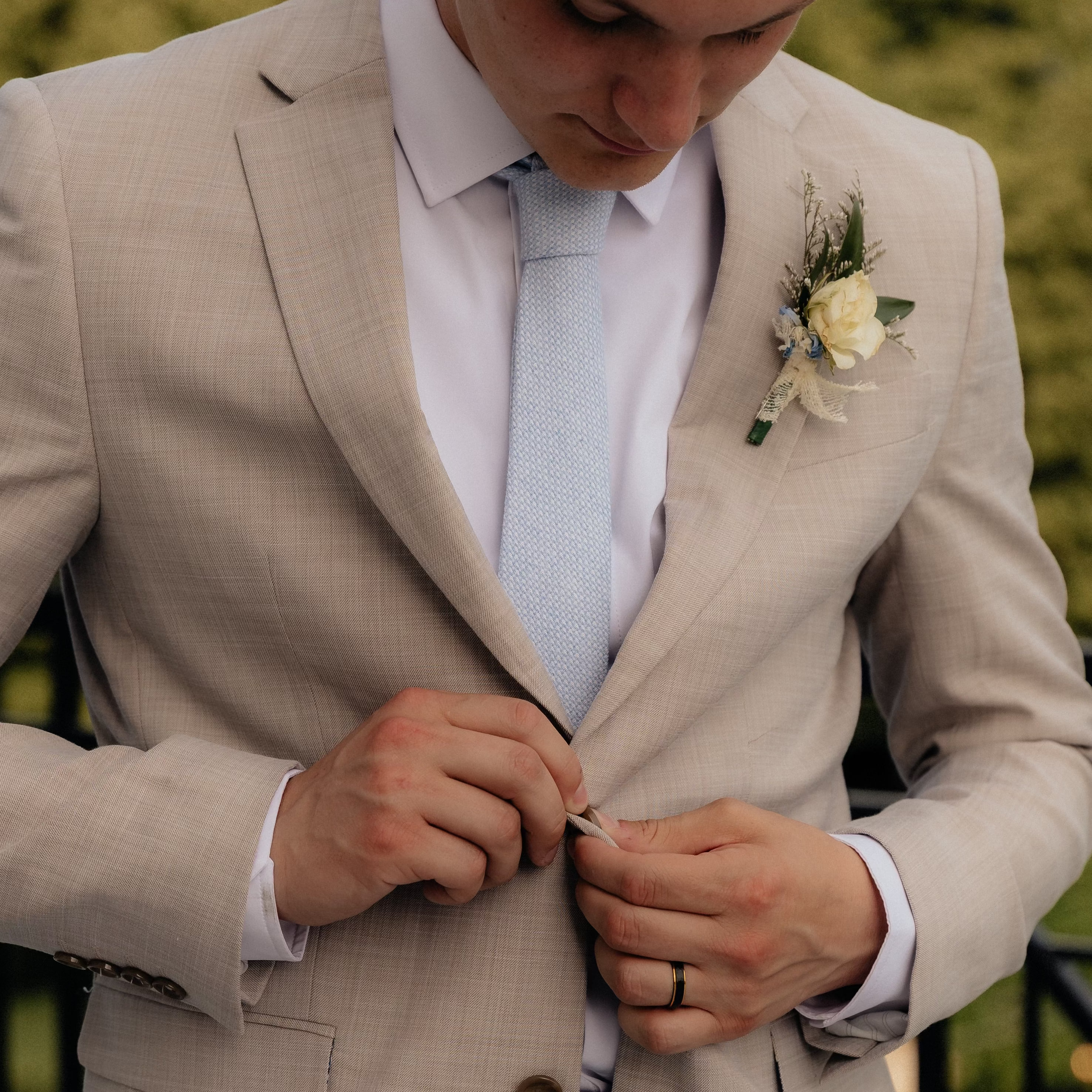 Groom in a knitted blue tie buttoning his suit
