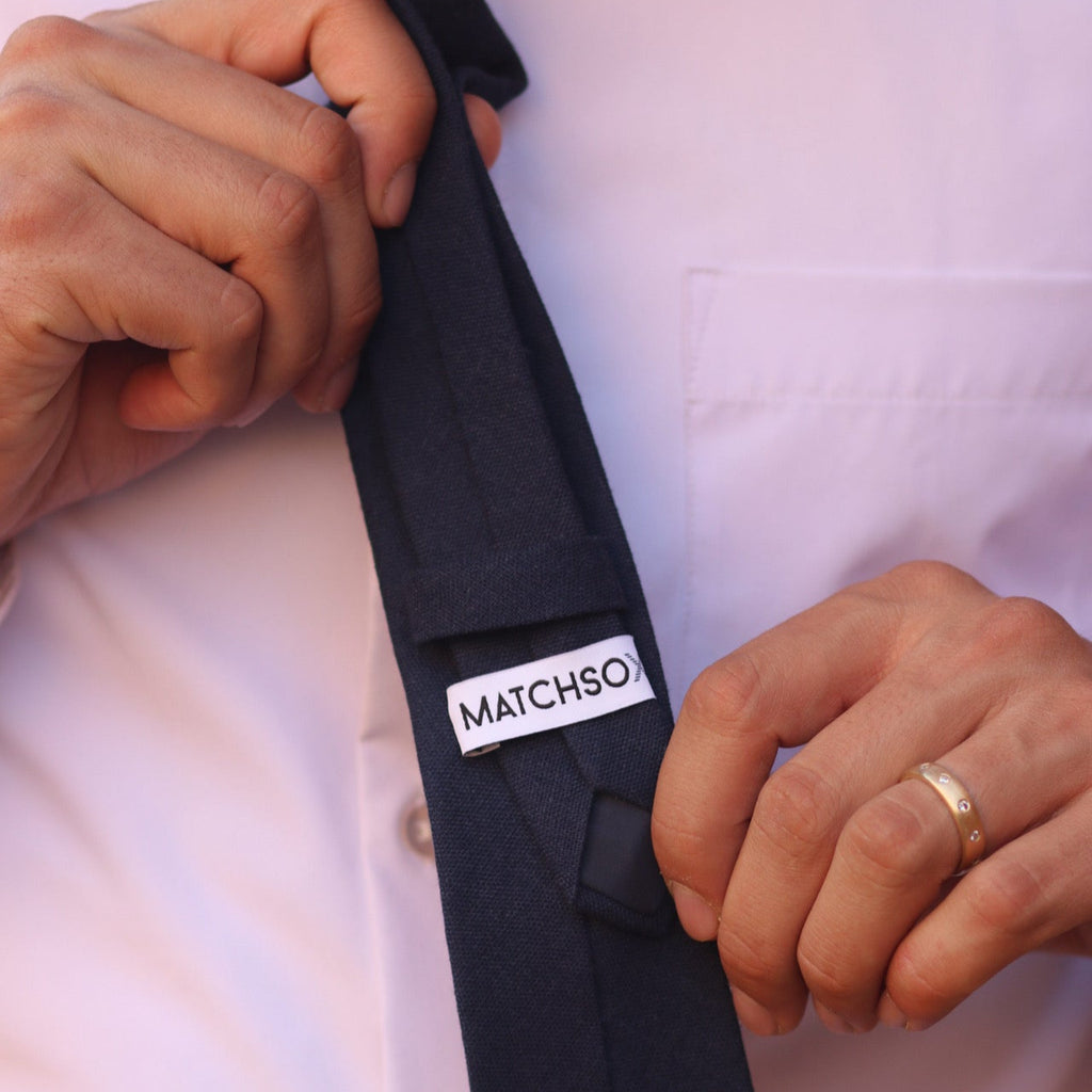 Person adjusting a navy blue tie with 'MATCHSOX' label on a white shirt background
