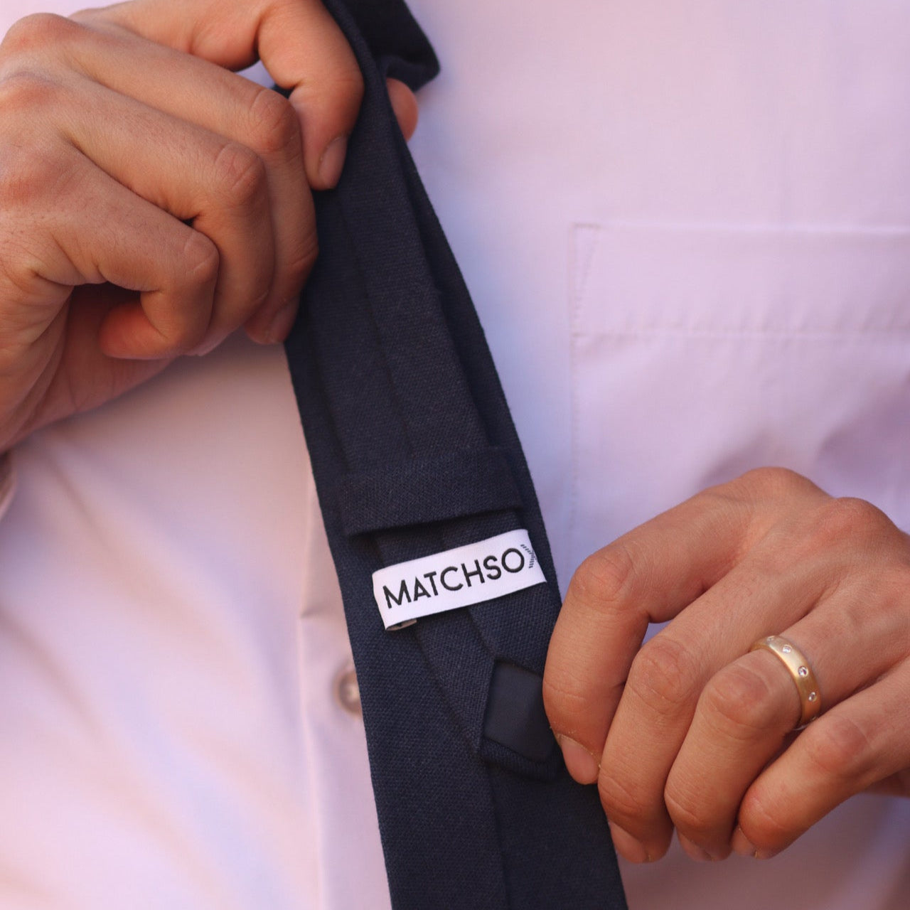 Person adjusting a navy blue tie with 'MATCHSOX' label on a white shirt background