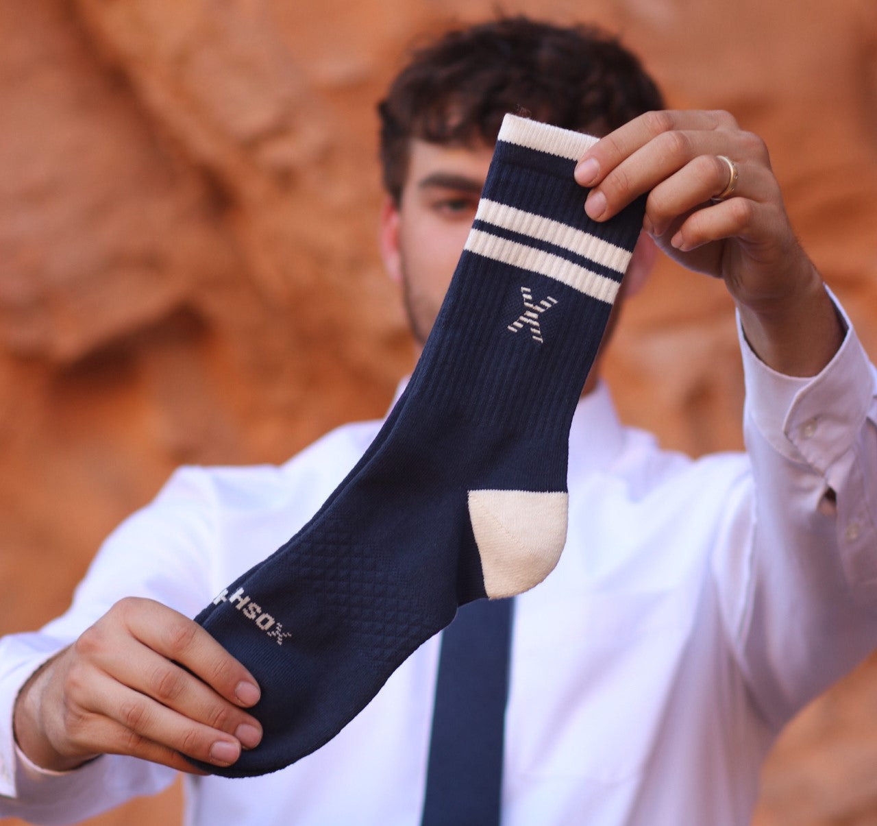 Person holding a navy dress sock with white stripes against a blurred natural background