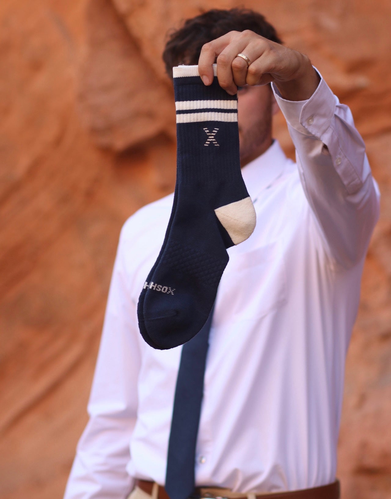 Person holding navy blue matchsox dress socks with white stripes against a red rock background