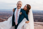 Man in a pink tie holding a woman in a wedding dress with a scenic background
