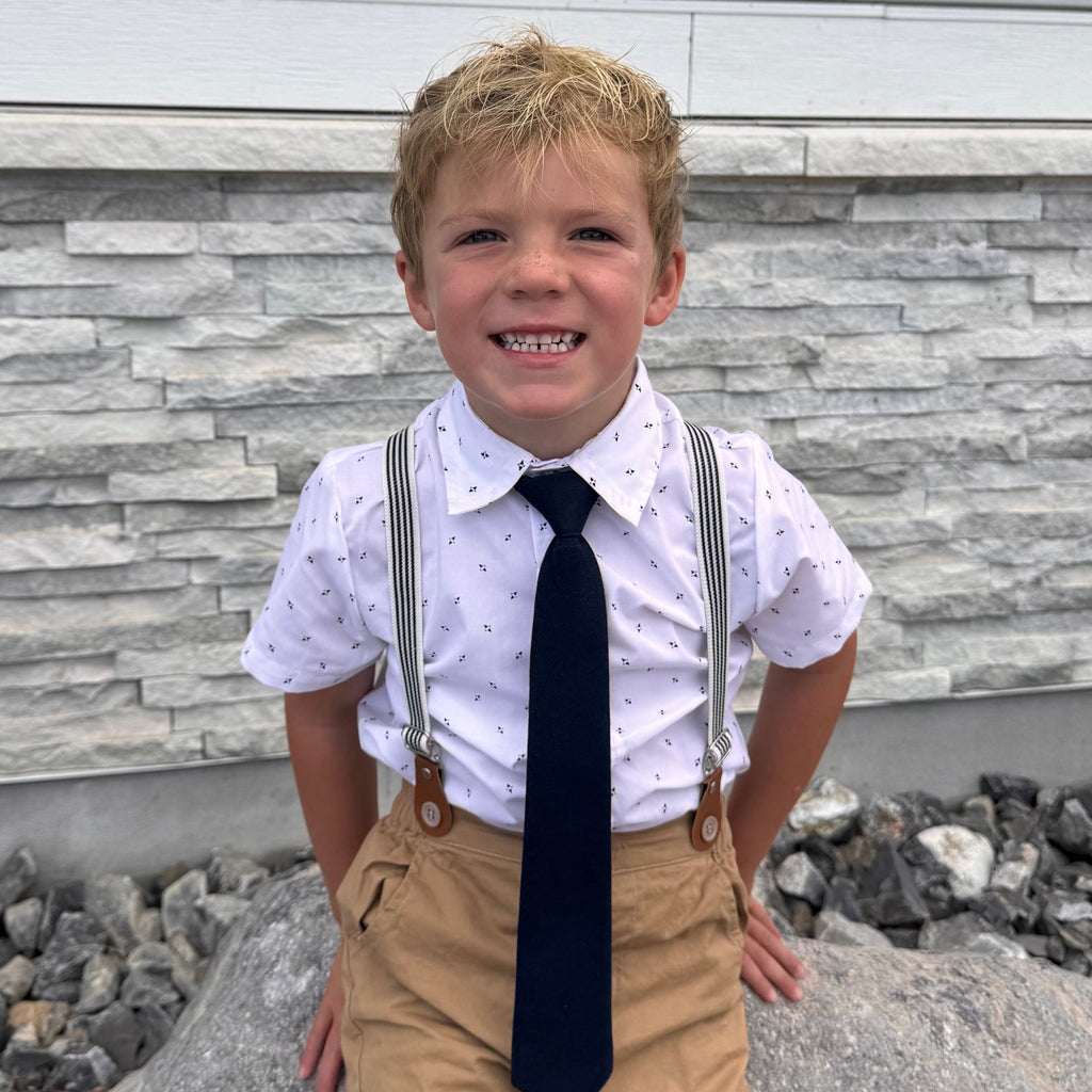 Child in a white shirt and tie standing on a stone pathway