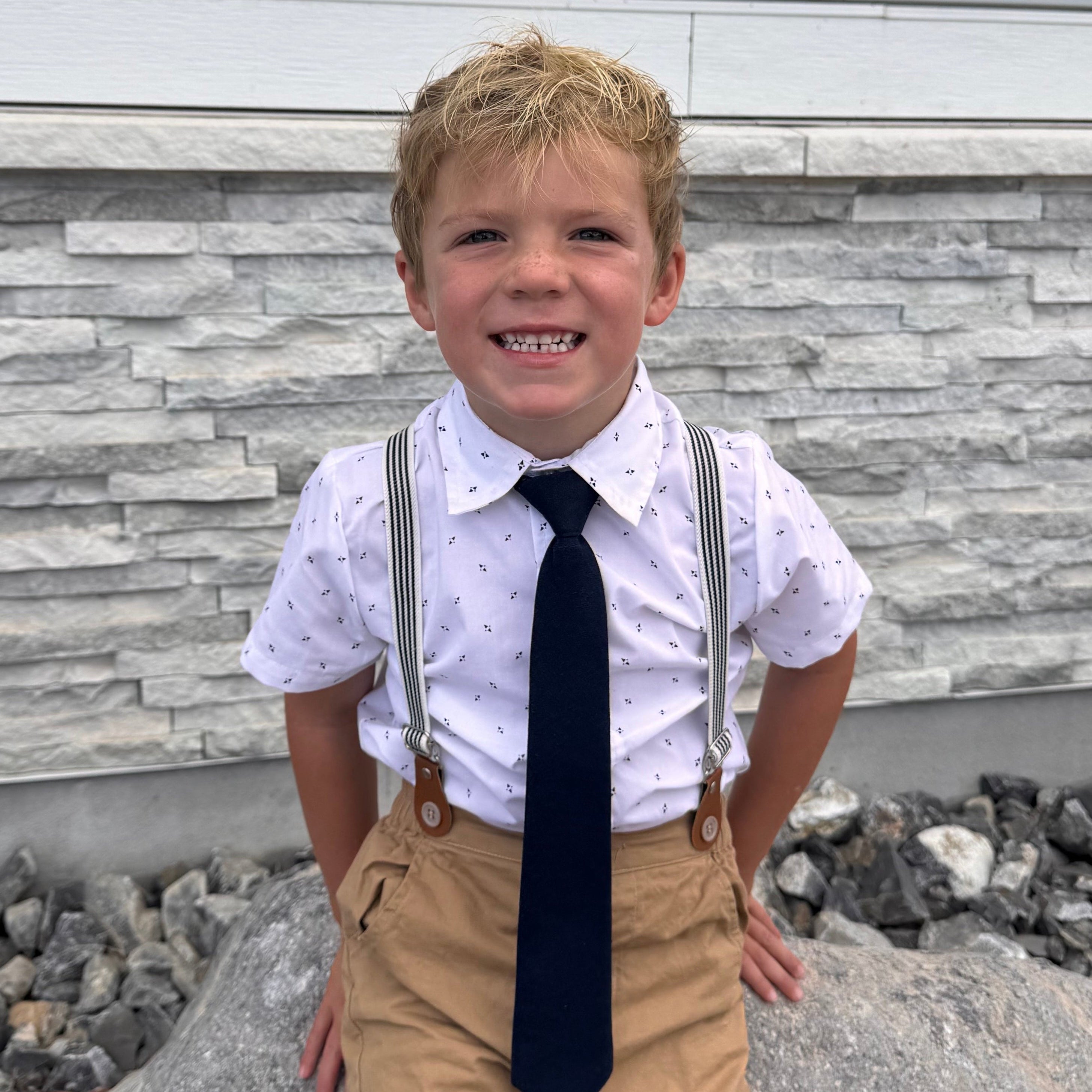 Child in a white shirt and tie standing on a stone pathway