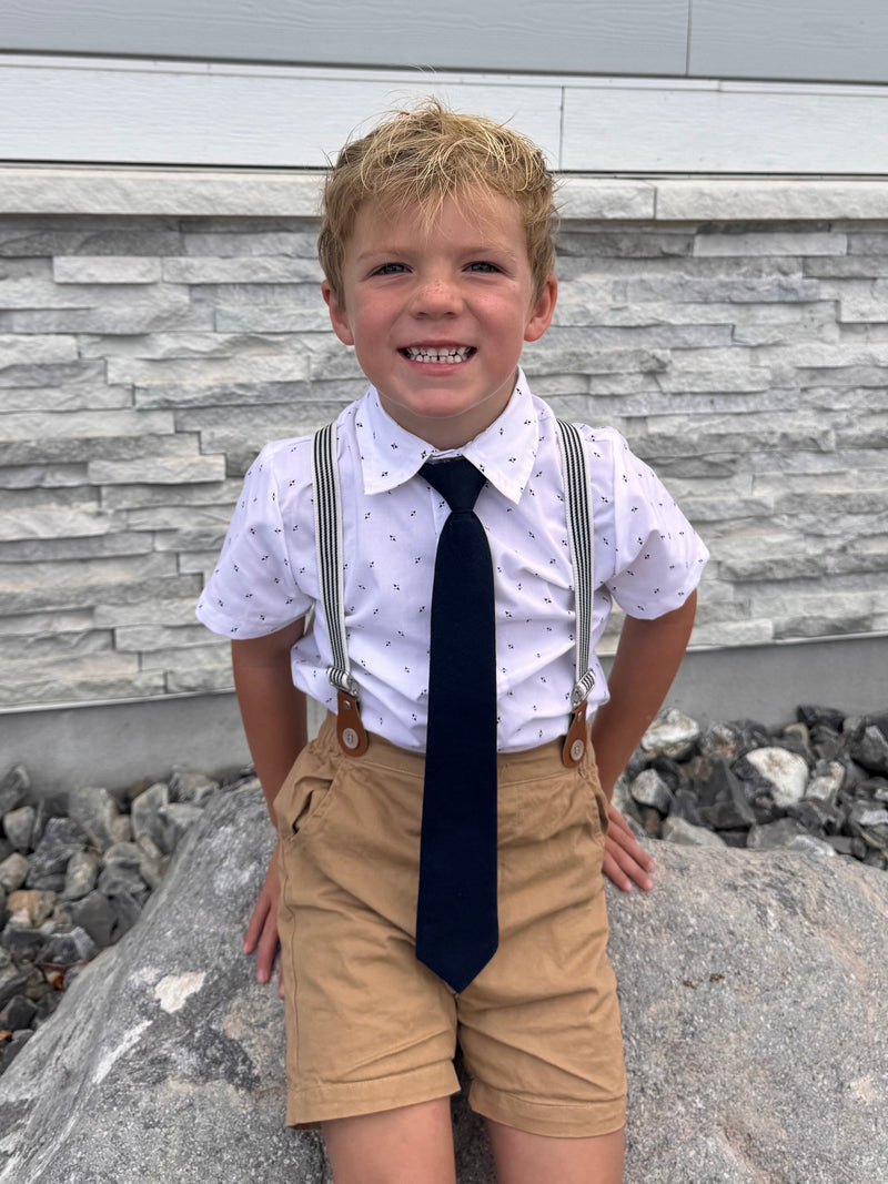 Child in a white shirt and tie standing on a stone pathway